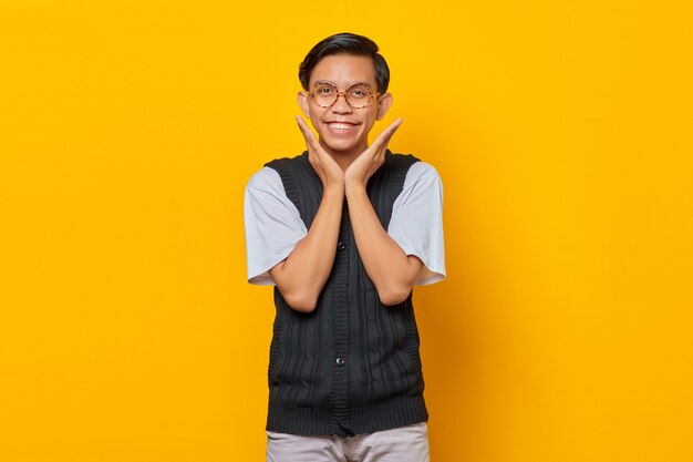 Portrait of cheerful asian young man looking camera on yellow background