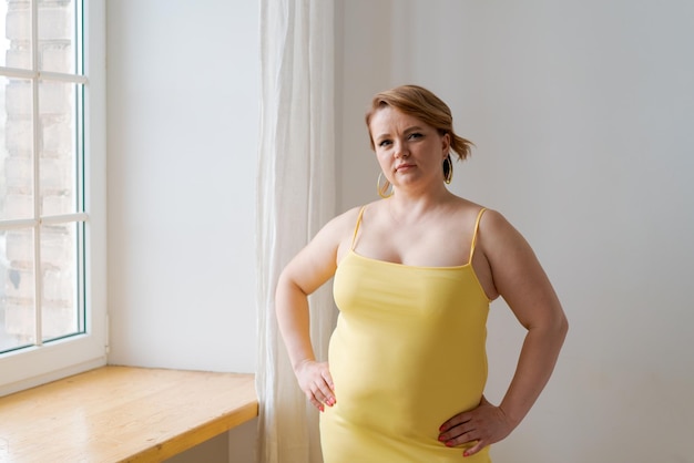 Portrait cheerful attractive young plump plus size woman in yellow tight dress looking at the camera...