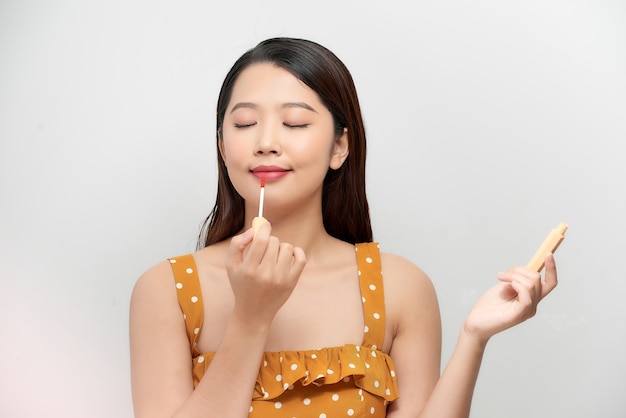 ピンクの口紅とマスカラのブラシを手にポーズと笑顔の孤立した白い背景で陽気な魅力的な若い女性の肖像画。