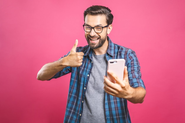 Portrait of a cheerful bearded man taking selfie and showing thumbs up gesture 