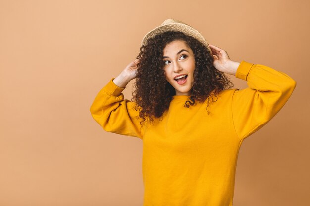 Portrait of a cheerful beautiful curly smiling girl in straw hat isolated over beige background.