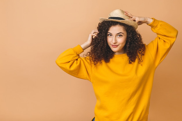 Portrait of a cheerful beautiful curly smiling girl in straw hat isolated over beige background.