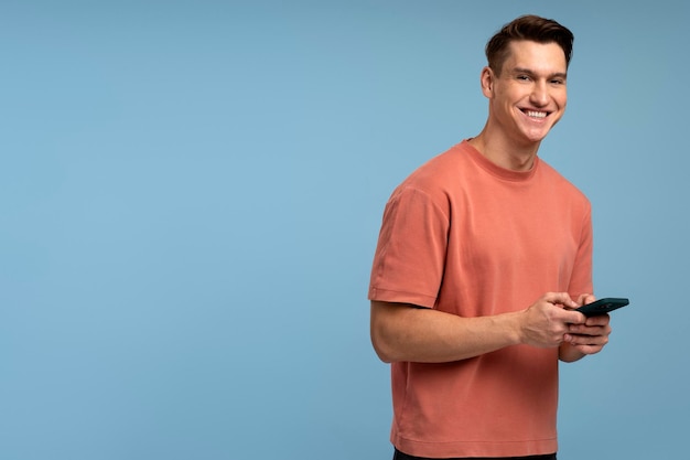 Ritratto di uomo brunetta allegro in maglietta utilizzando il cellulare e sorridente