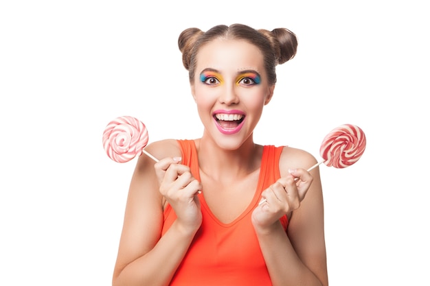 Portrait of cheerful brunette with two lollipops looking at camera with open mouth.