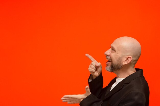 Portrait of a cheerful business man pointing to the side isolated on orange background person