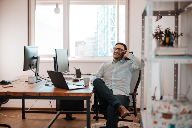 Portrait of cheerful businessman talking on phone in his office.