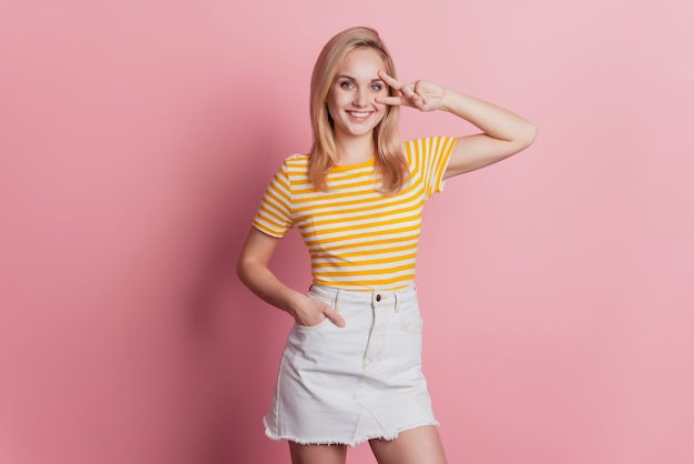 Portrait of cheerful charming lady cover eye v-sign on pink background