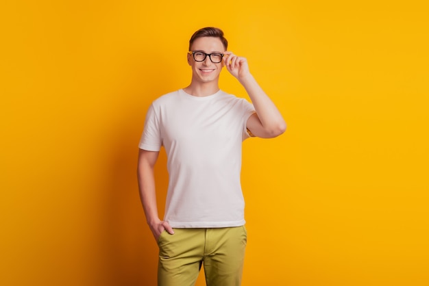 Portrait of cheerful charming nice attractive guy touch glasses look camera on yellow background