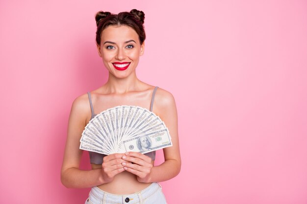 Il ritratto della lotteria di vittoria del fan dei soldi della tenuta della ragazza fiduciosa allegra gode del suo jackpot estivo indossa bei vestiti isolati sopra il colore rosa