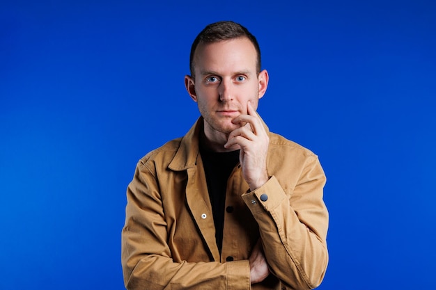 Photo portrait of a cheerful confident man on a blue background in a brown shirt the emotion of joy a man with a slight smile