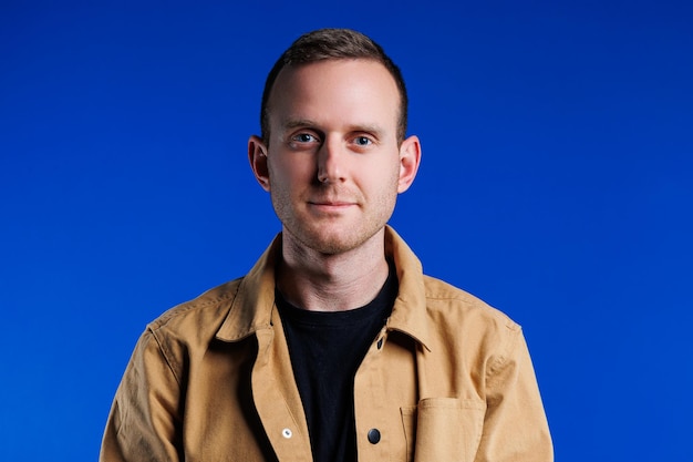 Portrait of a cheerful confident man on a blue background in a brown shirt The emotion of joy A man with a slight smile