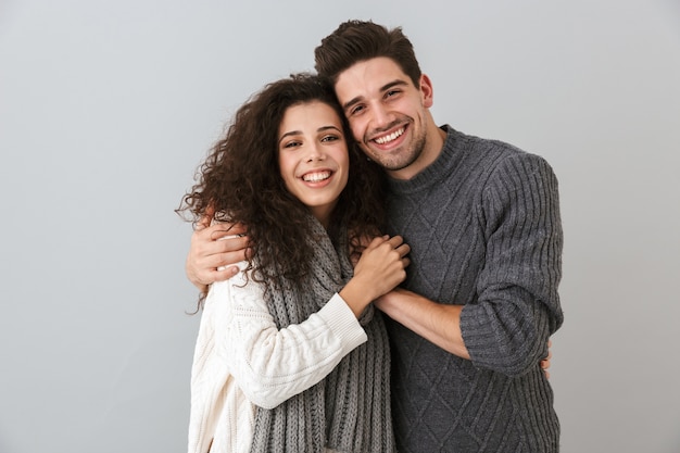 Portrait of cheerful couple man and woman smiling while hugging together, isolated over gray wall