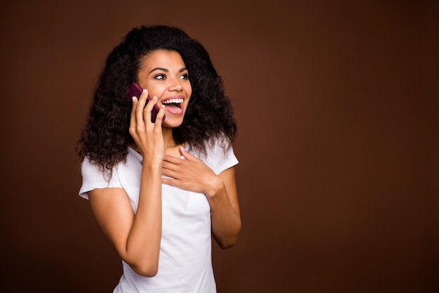 Portrait of cheerful crazy funny afro american girl use smart phone talk with her friends share incredible sales information wear white t-shirt.