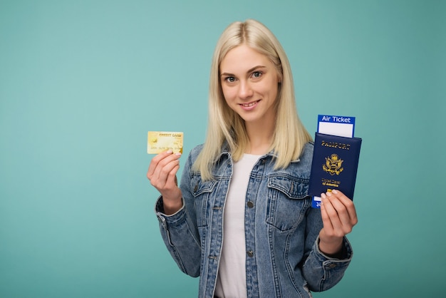 Portrait of a cheerful cute american girl traveller showing passport with air tickets and credit card