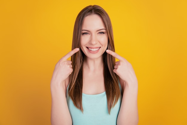 Photo portrait of cheerful cute lady indicate forefingers toothy beaming smile on yellow background