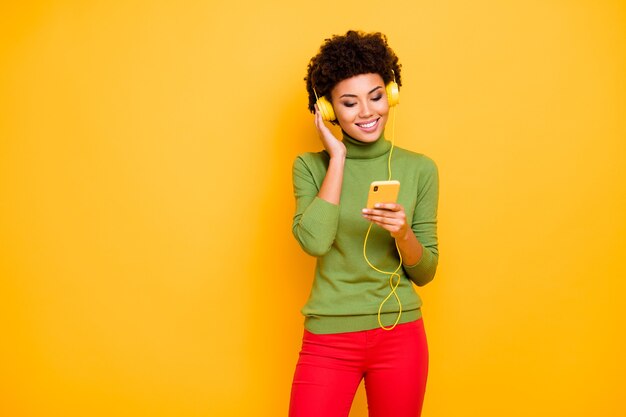 portrait of cheerful cute pretty nice woman in red pants green turtleneck curly wavy brown haired smile toothy downloading her favorite song while listening.