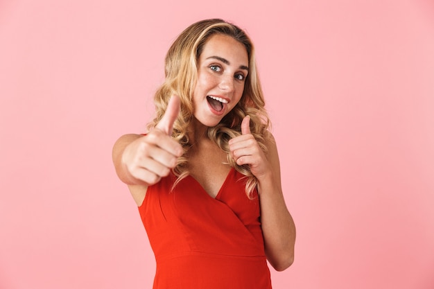 Portrait of cheerful cute young blonde woman posing isolated over pink wall make thumbs up gesture