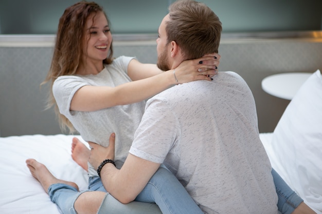 Portrait of a Cheerful cute young couple sitting in an embrace on a big bed