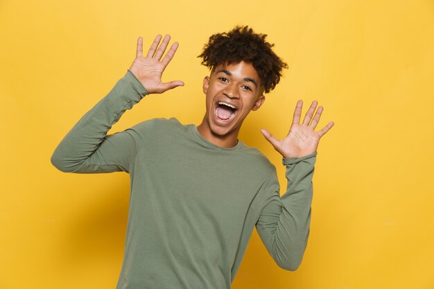 Photo portrait of cheerful dark skinned guy having stylish afro hairdo screaming or calling, isolated over yellow background