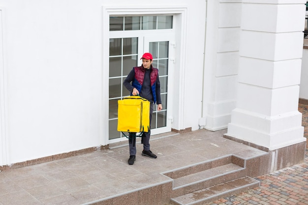 Portrait of a cheerful delivery man standing with yellow thermo backpack for food delivery on the street outdoors