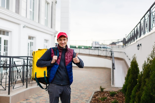 Portrait of a cheerful delivery man standing with yellow thermo backpack for food delivery on the street outdoors