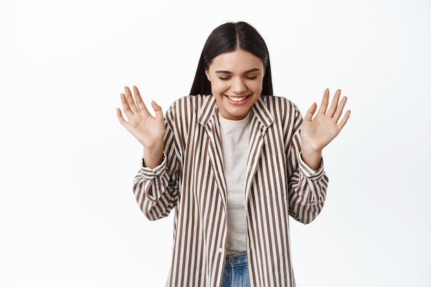 Portrait of cheerful dreamy woman close eyes and laugh, raising hands up happy, smiling with delight