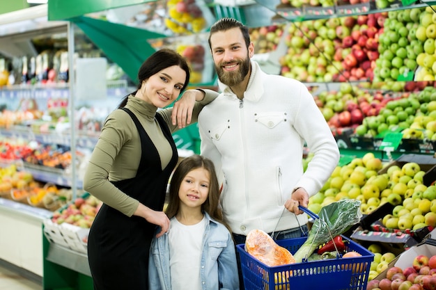 Ritratto di una famiglia allegra che sta con un carretto pieno nel supermercato nella verdura