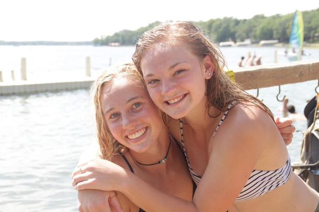 Portrait of cheerful female friends standing against lake