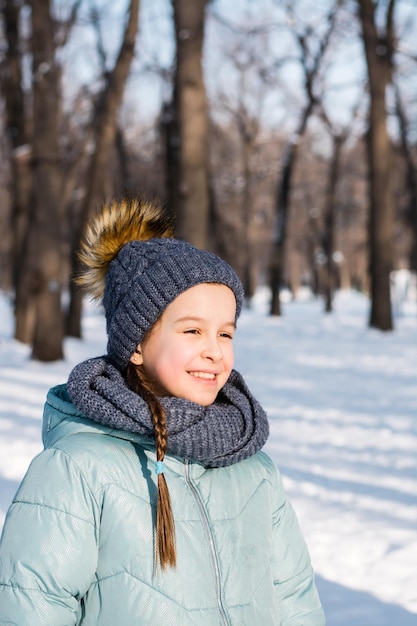 Portrait of a cheerful girl in warm clothes in a winter park on a frosty sunny day Vertical view