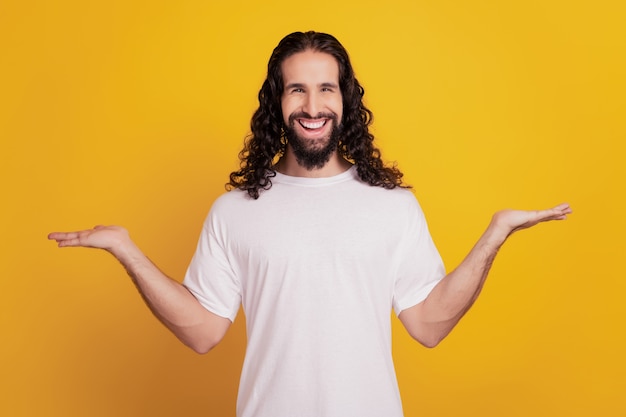 Portrait of cheerful guy palms hold invisible products compare novelty on yellow background