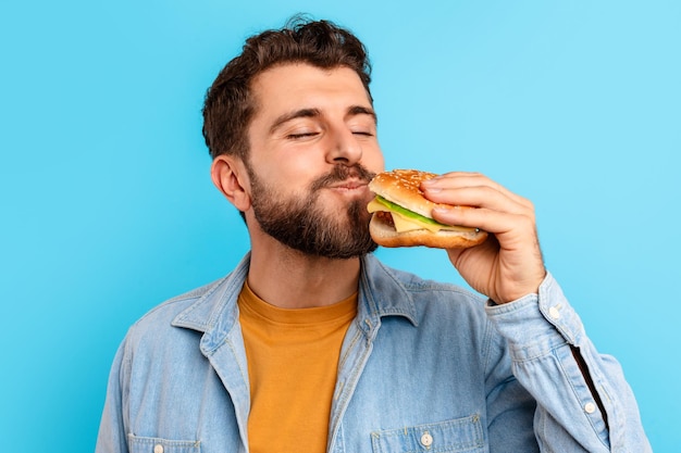 portrait of cheerful guy posing with burger eating big sandwich