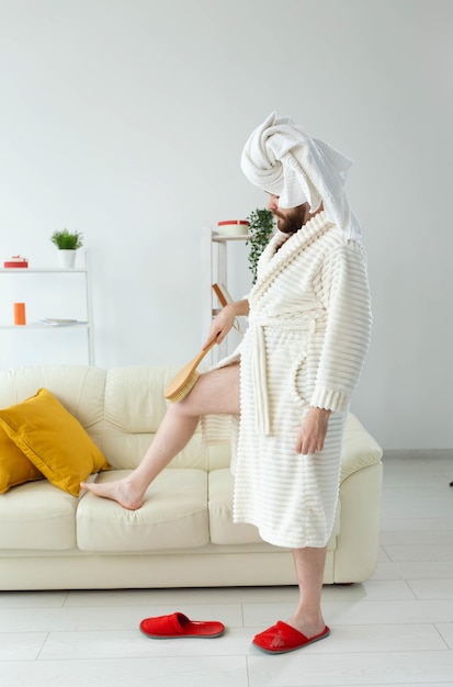 Portrait of cheerful guy wear turban towel makes himself a massage with massage brush. Male skin care and spa concept.