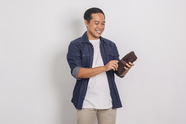 Портрет веселого красивого азиатского мужчины, заглядывающего в свой кошелек на белом фоне