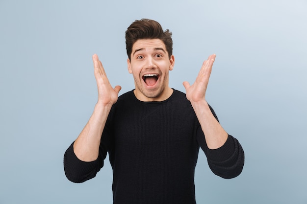 Portrait of a cheerful handsome young man standing isolated on blue, celebrating success