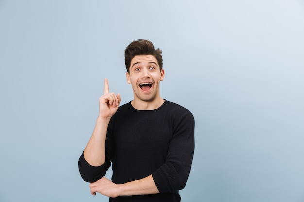 Portrait of a cheerful handsome young man standing isolated on blue, pointing at copy space