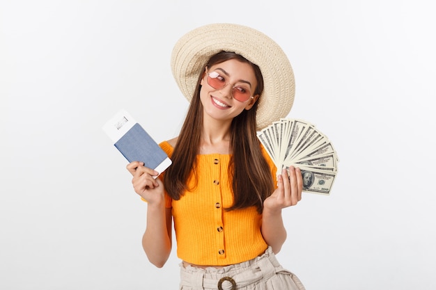 Ritratto della ragazza allegra, felice, di risata con il cappello sulla testa, avendo fan dei soldi e passaporto con i biglietti in mani, isolato su bianco