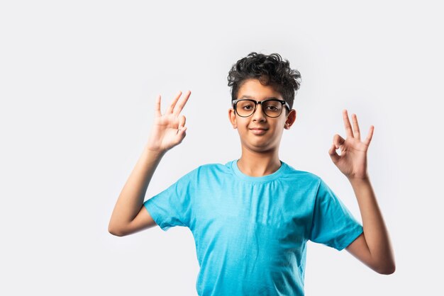 Portrait of cheerful Indian asian little boy with spectacles celebrating success standing against white wall