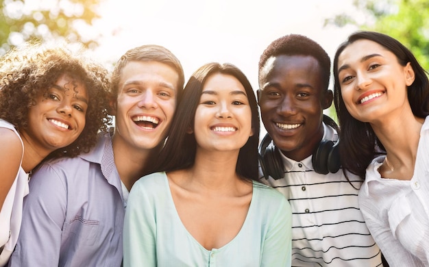portrait of cheerful interracial teen friends posing at camera outdoors smiling and laughing