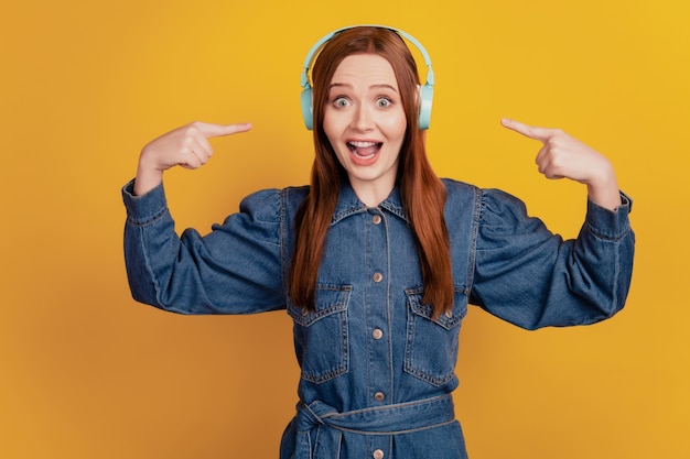 Portrait of cheerful lady wear headphones listen music direct fingers on yellow background