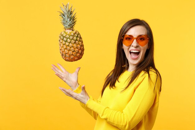 Portrait of cheerful laughing young woman in heart glasses pointing hands aside isolated on yellow orange wall background in studio. people sincere emotions, lifestyle concept. mock up copy space