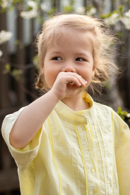 Портрет веселой маленькой девочки в желтом платье на фоне цветов