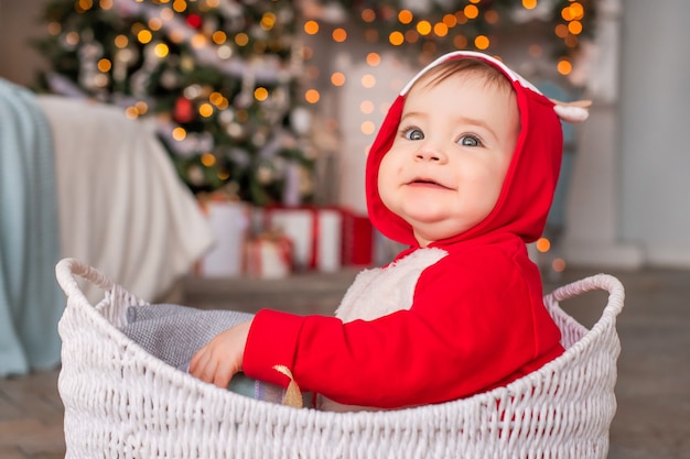 クリスマスツリーの背景にバスケットに座っているサンタクロースの赤いトナカイの衣装で陽気な小さな子供たちの肖像画