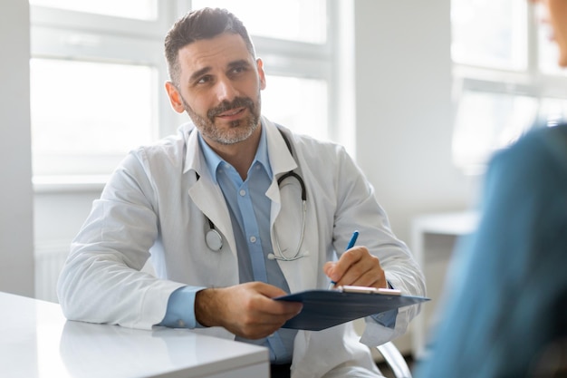 Portrait of cheerful male doctor listening to female patient discussing diagnosis and treatment