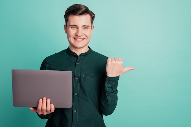 Portrait of cheerful man hold laptop direct thumb empty space on teal background