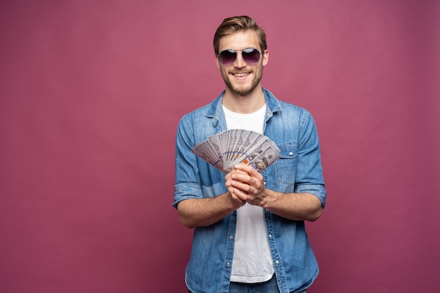 Portrait of a cheerful man holding dollar bills over pink background.