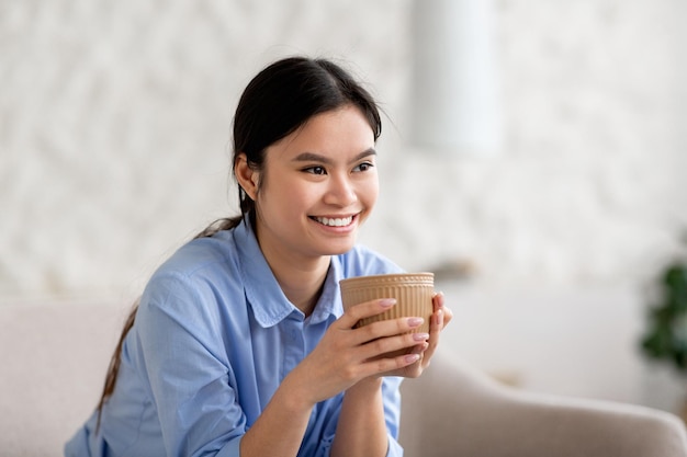 Portrait of cheerful millennial asian woman drinking tea