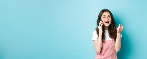 Portrait of cheerful modern girl talking on phone gesturing and looking happy smiling at camera chat