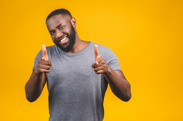 Portrait of cheerful, positive, handsome man with black skin, beaming smile in casual showing thumb up with finger to the camera isolated on yellow wall.