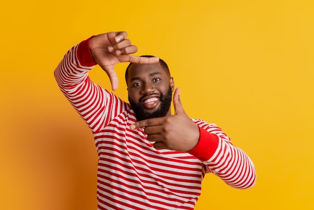 Portrait of cheerful positive man make frame with fingers on yellow wall