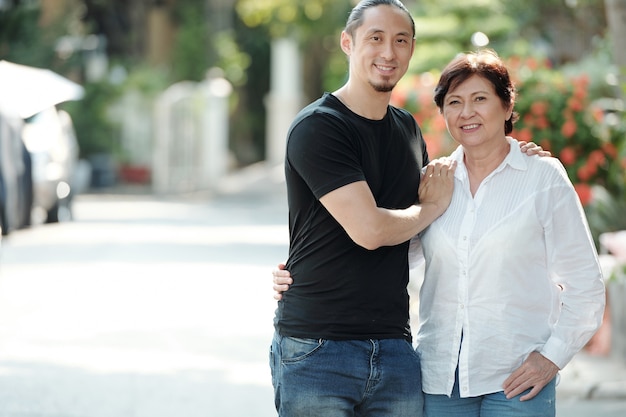 Portrait of cheerful pretty mature mixed-race woman and her adult son standing outdoors